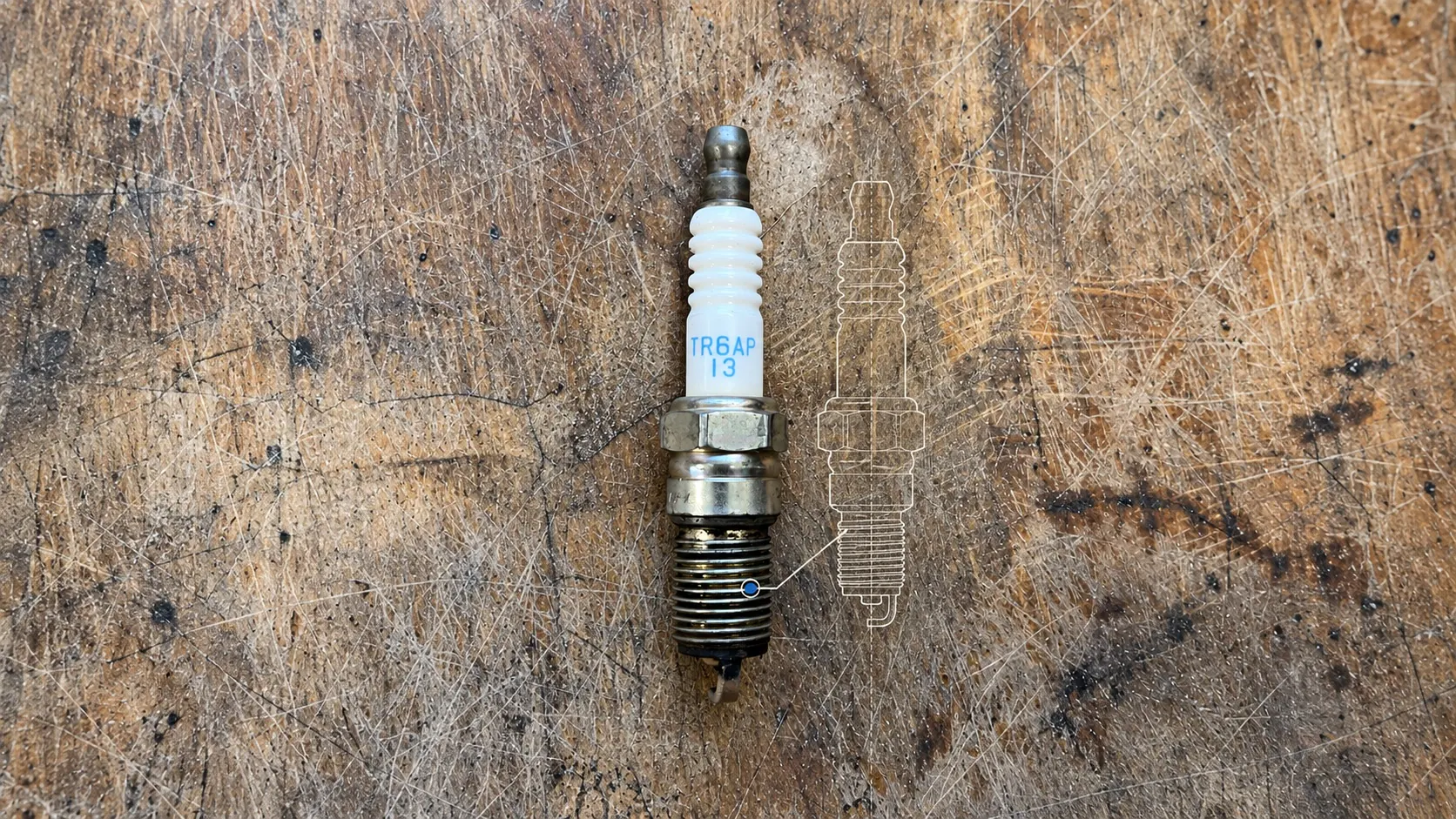 Te korte, gebruikte bougie uit een Volvo V70R op een bekraste houten werkbank